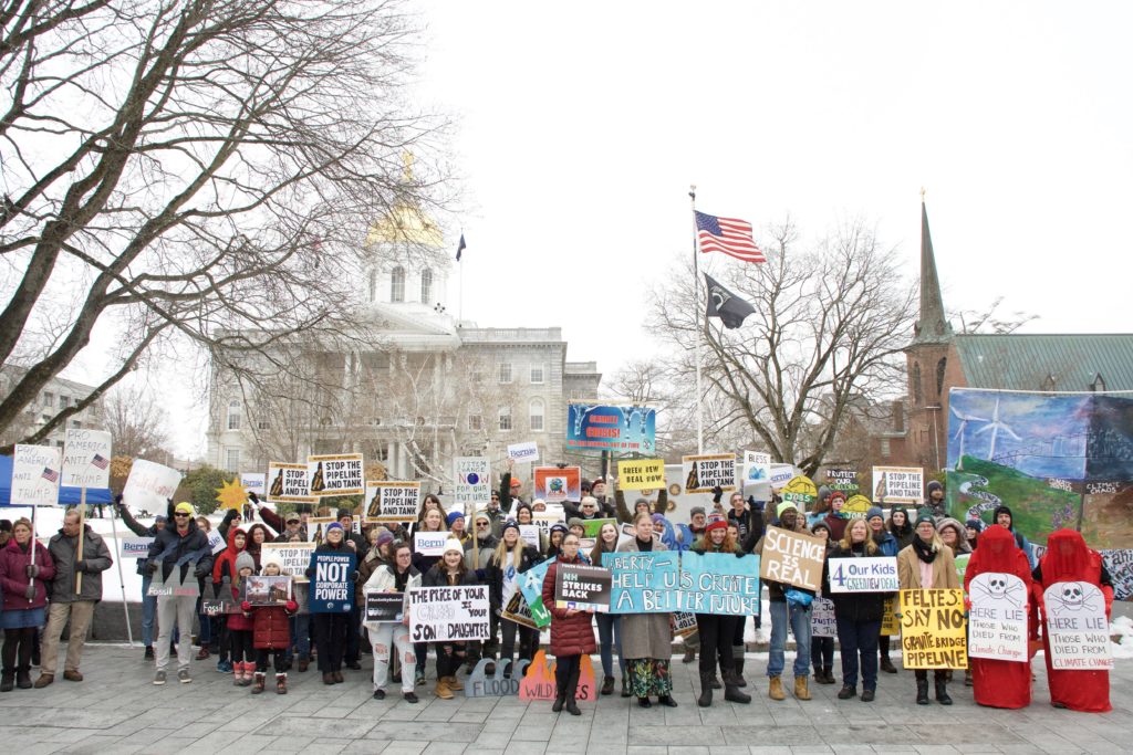 photo of a crowd in front of the state house with climate themed signs including some that say stop the pipeline and tank!